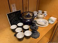 Group shot of twin-spout tea pot, six cups, plates, decorative vases, and Birks candlesticks on wooden shelf