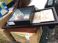 Photo showing the stacked shadow boxes and framed art pieces on a box outdoors.