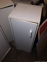 White melamine cabinet with single door, white handle, showing minor surface wear.