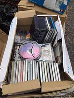 Full box showing a mix of sealed music CDs in jewel cases and a spindle of blank CDs