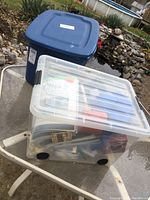 Two plastic totes placed outdoors, one clear with visible contents, one blue closed tote