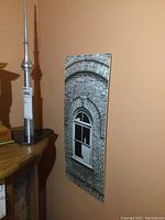 Photo showing the aluminum CN Tower model next to the black and white brick building print on a wall.