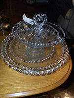 Stacked glass serveware pieces showing the beaded edge and pedestal base on the largest plate with heart-shaped beaded handle.