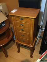 Front view of wood jewelry chest on stand showing curved top, four drawers with brass-tone handles.
