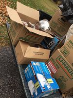 Photo of multiple cardboard boxes on outdoor surface containing kitchen ware and small appliances like food processors.