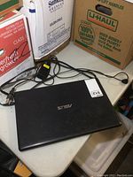 Closed Asus laptop on table with charger cable and plug visible