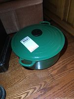 Green Le Creuset round pot with lid shown from an angle on a wooden floor