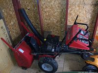 Front view of snow blower showing red housing, chute and attached shelter canopy