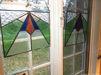 Photo showing two stained glass panels hanging side by side in front of a window, measuring approximately 16x16 and 17x13 inches