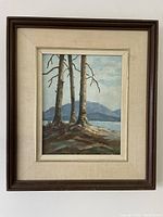 Framed oil painting showing three trees in a lakeside or seaside landscape with hills or mountains in the distance under a sky with clouds.