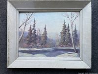 Full view of the signed oil painting on masonite depicting a winter landscape with snow, trees, and a frozen or reflective water surface in a white wooden frame.