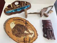 Four pieces of wood art and carvings displayed including an eagle plaque, wood tree carving, carved pipe, and a carved face piece.