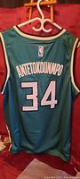 Back of a teal Milwaukee Bucks basketball jersey showing the name 'ANTETOKOUNMPO' and number 34 in white with NBA logo on the top.