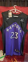Front view of black and purple Toronto Raptors basketball jersey with number 23 and Raptors text, showing tags unopened.