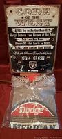 Photo of Dodge branded tin sign with 'Code of the West' text and RAM logo, along with a packaged Dodge T-shirt size L.