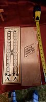 Vintage Curtis cribbage counter beside a measuring tape showing approximately 10 inches in length, along with the original box with the label.