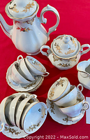 Photo of coffee pot, sugar bowl, creamer, demitasse cups and saucers with white porcelain and gold floral design