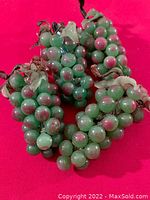 Four bunches of Murano glass grapes with green and pink beads attached to stems with glass leaves on red background.