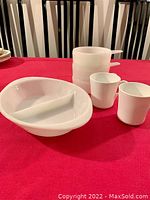 Three white milk glass soup bowls with handles and one oval divided oven dish on red tablecloth, showing the entire lot.