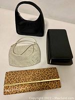 Four handbags arranged flat: black small shoulder bag, white textured bag, black wallet clutch, leopard print clutch.