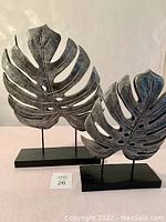 Two metal leaf sculptures on black bases shown side by side.