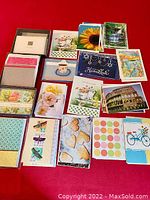 Overview of greeting card assortment arranged on red surface showing variety of designs including flowers, animals, scenic images, and patterns.