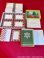 Photo showing stack of postcards with matching envelopes, and two boxes: one with cartoon holiday cards and the other with snowflake design cards.