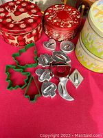 Four decorated round cookie tins with various Christmas and Easter themes alongside a collection of metal and plastic cookie cutters including Christmas tree shapes and other holiday shapes.