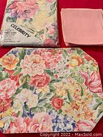Floral octagonal placemat and folded pale pink linen napkins displayed alongside packaged tablecloth.