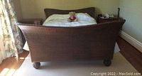 Full view of the wicker queen sleigh bedframe showing its curved footboard and part of the headboard in a bedroom setting.