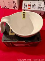 White ceramic spoon holder in a unique curved shape, placed on top of its box.