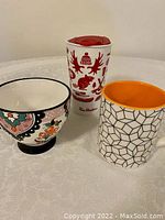 Photo showing three coffee cups/mugs including a floral patterned cup, Tim Hortons travel cup, and geometric patterned mug with orange interior