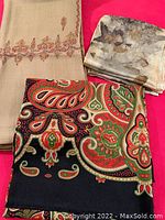 Three scarves displayed on red background showing beige printed scarf with red border, black and red paisley scarf, and hand dyed leaf motif silk scarf.
