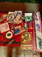 Photo of assorted tools and hardware including sockets, plastic packs, brass caps, coiled steel tape, thermostat, and wrench.