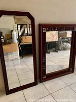 Two wood framed mirrors, one large reddish-brown with carved details and another smaller rectangular with dark finish.