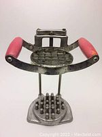 Front view of vintage French fries cutter showing red handles and sharp blades.