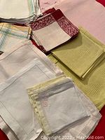 Close-up of folded vintage linen napkins and tea towels of various colors and patterns on a red surface.