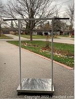 Full view of the metal clothing rack on wheels standing outdoors showing the rectangular base and adjustable clothes bar.