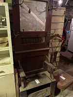 Full frontal view of antique hall coat tree showing the mirror, hooks, and seat with storage space underneath. The item is positioned in a dimly lit basement area.