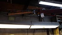 Long view of multiple fishing rods horizontally stored on a wooden rack attached to ceiling beams, showing rods with fishing reels near the base.