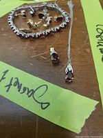 Full view of bracelet, multiple pairs of earrings, and two necklaces with garnet pendants on a wooden surface with a green tape label.