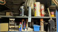 Shelf with various aerosol cans including WD-40, sprocket lubricant, decal remover, spray paint, and blue plastic container.