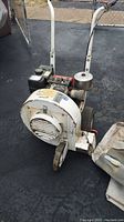 Full side view of white Briggs and Stratton leaf blower with attached bag, showing engine, handle, wheels, and shroud with rust and paint wear.