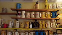 Full view of six wooden shelves laden with assorted collectible mugs in various colors and designs including fantasy and brewery logos.