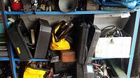 Photo of blue metal shelving showing multiple black tool cases, a yellow tool pouch, and other boxes with power tools inside.