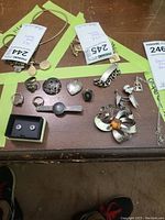 Photo shows spread of sterling silver jewelry including rings, brooches, bracelets, pendant, earrings, and tie bar arranged on a wooden board with inventory tags visible.