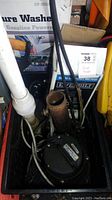 Overview photo showing three sump pumps including one black Everbilt pump in box with visible power cord and discharge pipe, surrounded by other items in storage.