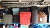 Photo showing the assortment of 8 tool boxes of various sizes and colors, mainly plastic, arranged against a wall in a garage. The distinctive vintage brown leather or leatherette box is on the right.