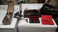 Wide shot of all items in the lot including Craftsman planar, nail tool, sockets, and screwdriver bit sets on top of a white appliance.