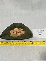 Top-down view showing the triangular shape and central hand-painted flower on dark green background.
